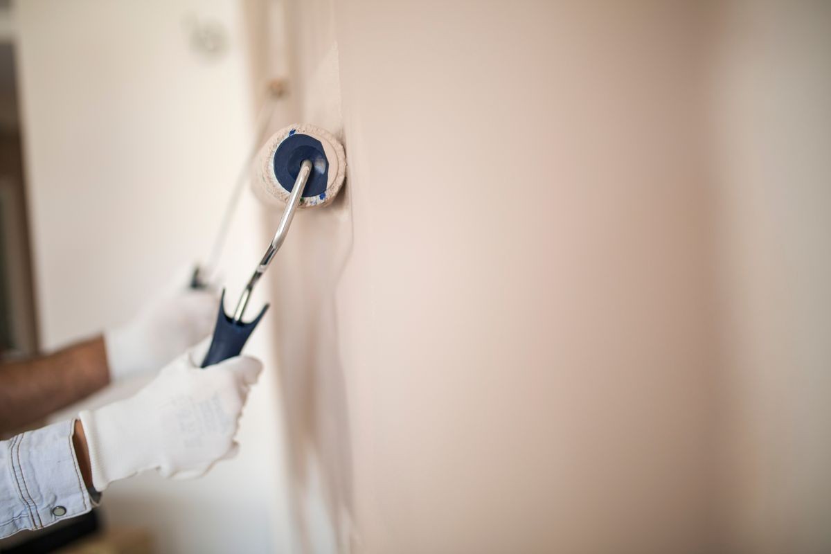 Close up of a hand with glove holding painting roller and painting wall in light brown color.