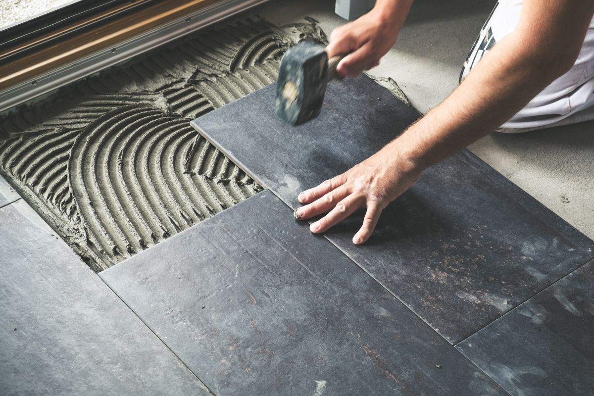 Worker placing ceramic floor tiles on adhesive surface